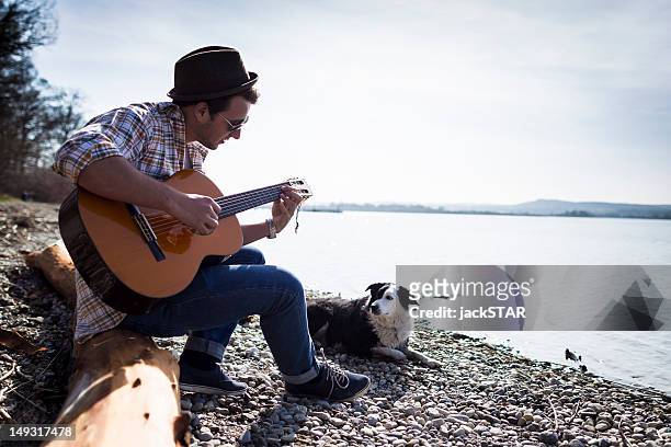 man playing guitar with dog by creek - outdoor guy sitting on a rock stockfoto's en -beelden