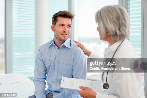 doctor talking to man in office - man touching shoulder stock-fotos und bilder