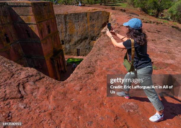 European tourist taking picture of St Georges rock-hewn church from the top, Amhara Region, Lalibela, Ethiopia on May 2, 2023 in Lalibela, Ethiopia.