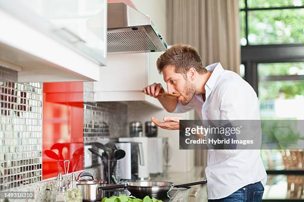 man tasting food in kitchen - goûter photos et images de collection