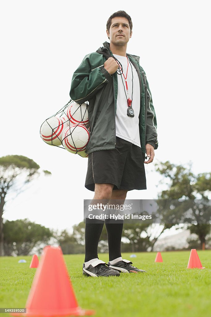 Coach carrying soccer balls on pitch