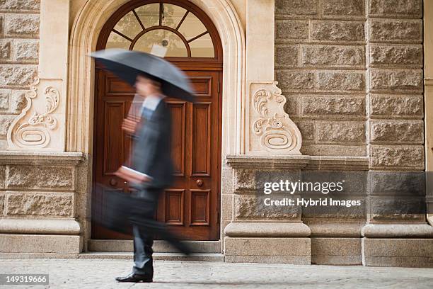 businessman carrying umbrella on street - toewijding stockfoto's en -beelden