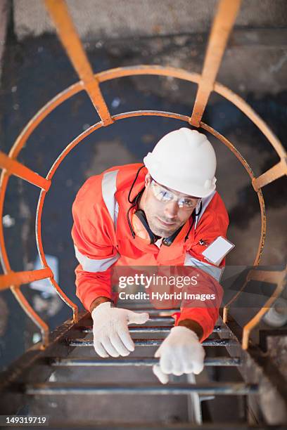 worker climbing ladder at oil refinery - raffinerie photos et images de collection
