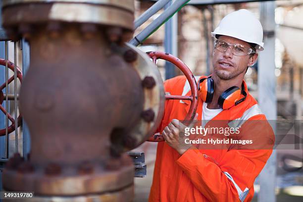 worker adjusting gauge at oil refinery - oliewerker stockfoto's en -beelden