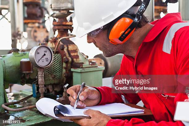worker noting gauge at oil refinery - chemical engineering stock-fotos und bilder