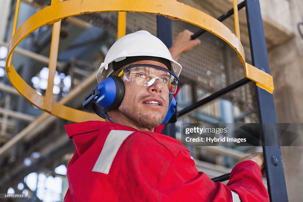 Worker climbing ladder at oil refinery