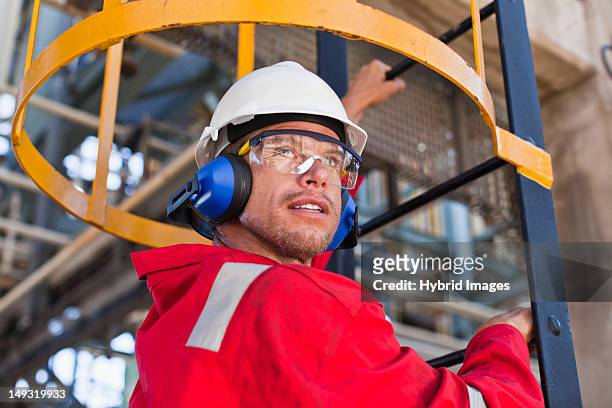 worker climbing ladder at oil refinery - sports helmet stock pictures, royalty-free photos & images