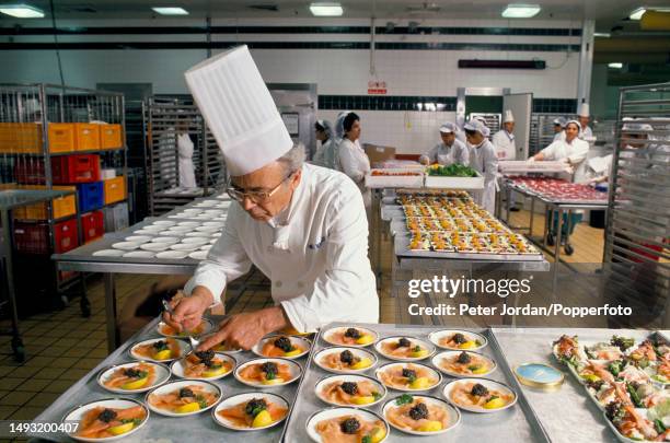 An executive chef distributes portions of caviar onto dishes for consumption by airline passengers in a kitchen prep area at British Airways Catering...