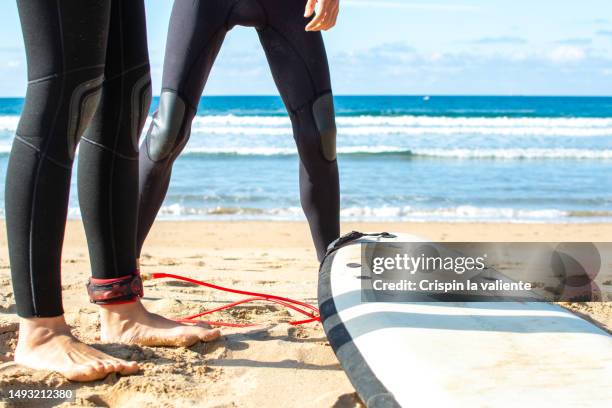 low angle of two surfers with wetsuit and surfboard on beach shore - neopren stock-fotos und bilder