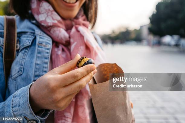 young woman eating roasted chestnuts on the street in istanbul - chestnut food stockfoto's en -beelden