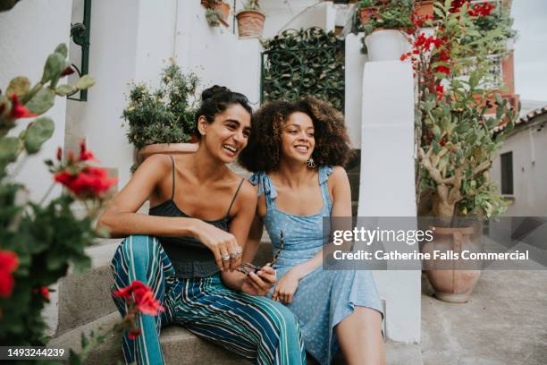 two pretty woman relax on a european style apartment stoop - they laugh - mediterranean culture stock pictures, royalty-free photos & images