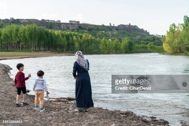 siblings playing by the tigris river in the city landscape of diyarbakir surrounded by historical walls and their mother next to them - tigris river stock pictures, royalty-free photos & images