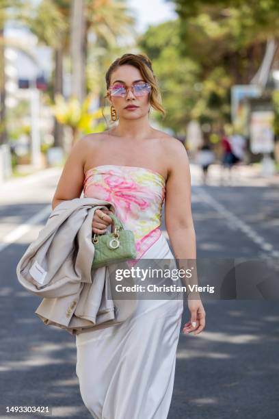Merve Görg�öz wears beige oversized blazer, white skirt, off shoulder top with print, green Dior bag, Fen earrings, Fendi sunglasses during the 76th...