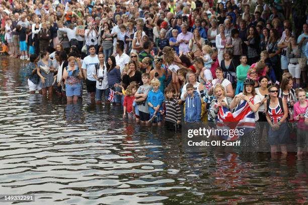 Crowds enter the water to watch the Queen's rowbarge 'Gloriana' carry the Olympic flame along the river Thames from Hampton Court to City Hall on the...