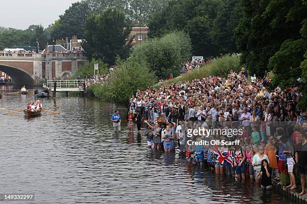 Crowds enter the water to watch the Queen's rowbarge 'Gloriana' carry the Olympic flame along the river Thames from Hampton Court to City Hall on the...