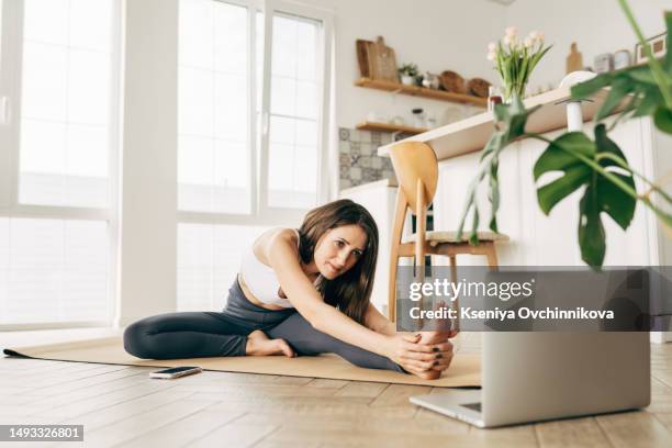 fit woman in sportswear doing yoga on exercise mat at home using laptop watching tutorial. female coach has a virtual yoga class on computer. healthy and active lifestyle concept. online home training - sporting training and press conference stock pictures, royalty-free photos & images