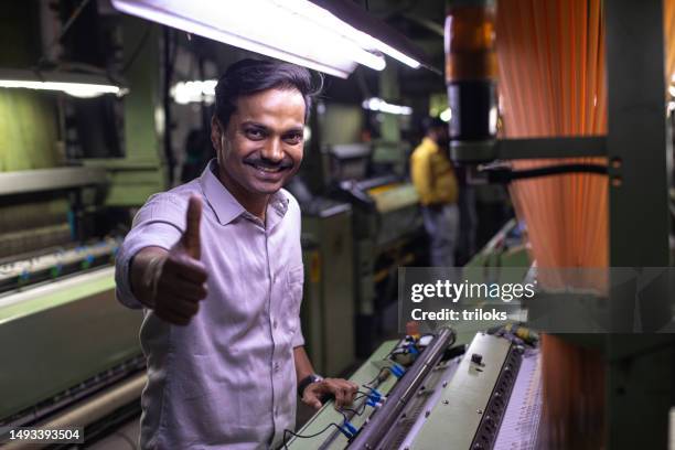 arbeiter zeigt daumen-hoch-zeichen, während er ausrüstung in textilfabrik benutzt - ok werk stock-fotos und bilder