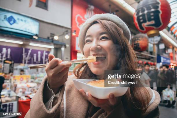 eine asiatin schwelgt in der japanischen küche und genießt die aromen von oden, einer beliebten lokalen delikatesse, auf dem geschäftigen kuromon-markt in osaka. - taiwanesischer abstammung stock-fotos und bilder