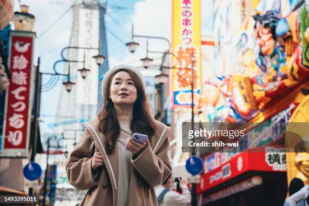 una donna asiatica sta visitando osaka, in giappone. cammina lungo la via dello shopping di fronte a tsutenkaku, ammirando l'atmosfera giapponese unica e gli aspetti culturali distintivi di osaka. - osaka shinsekai food foto e immagini stock