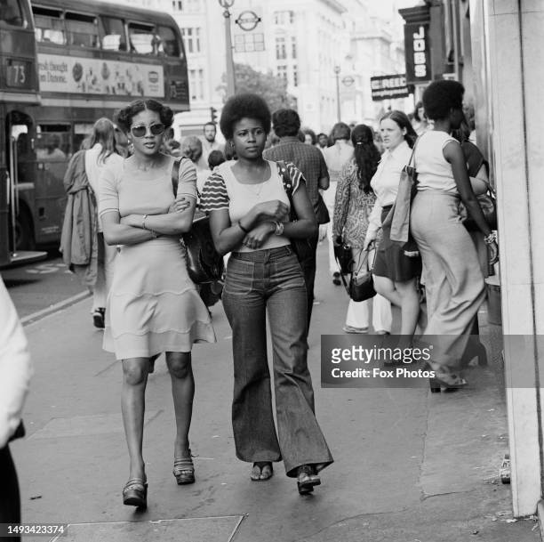 Two women walking along a pavement in London's West End, with other shoppers and tourists in the background, September 17th 1973.