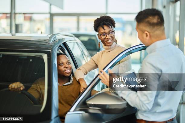 feliz pareja negra hablando con un vendedor de autos en una sala de exposición. - car ownership fotografías e imágenes de stock