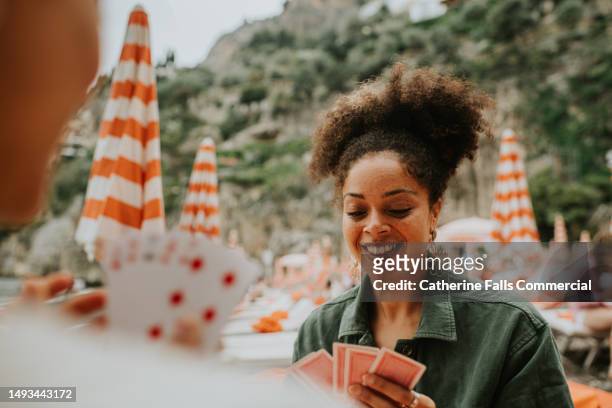 happy woman enjoy a game of cards on a beach. - solitaire stock pictures, royalty-free photos & images