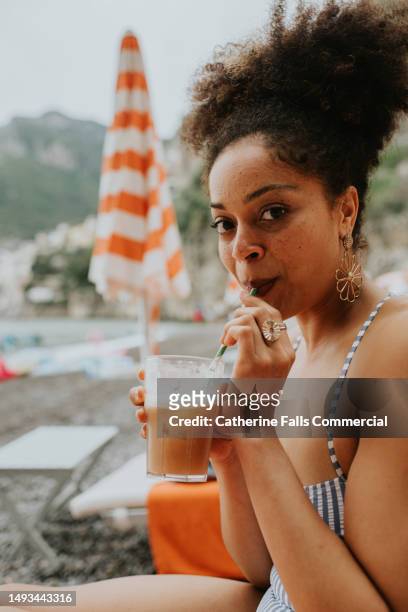 a woman sips juice from a straw on a beach - refresh stock pictures, royalty-free photos & images