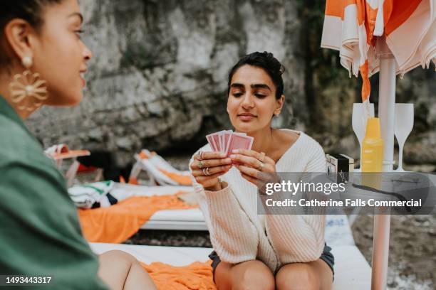 two woman play a game of cards on a beach - solitaire stock pictures, royalty-free photos & images