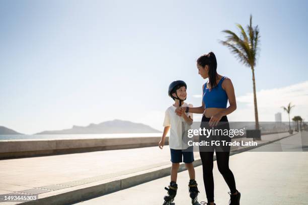 madre ayudando a su hijo a patinar en la costa de una playa - mothers day beach fotografías e imágenes de stock