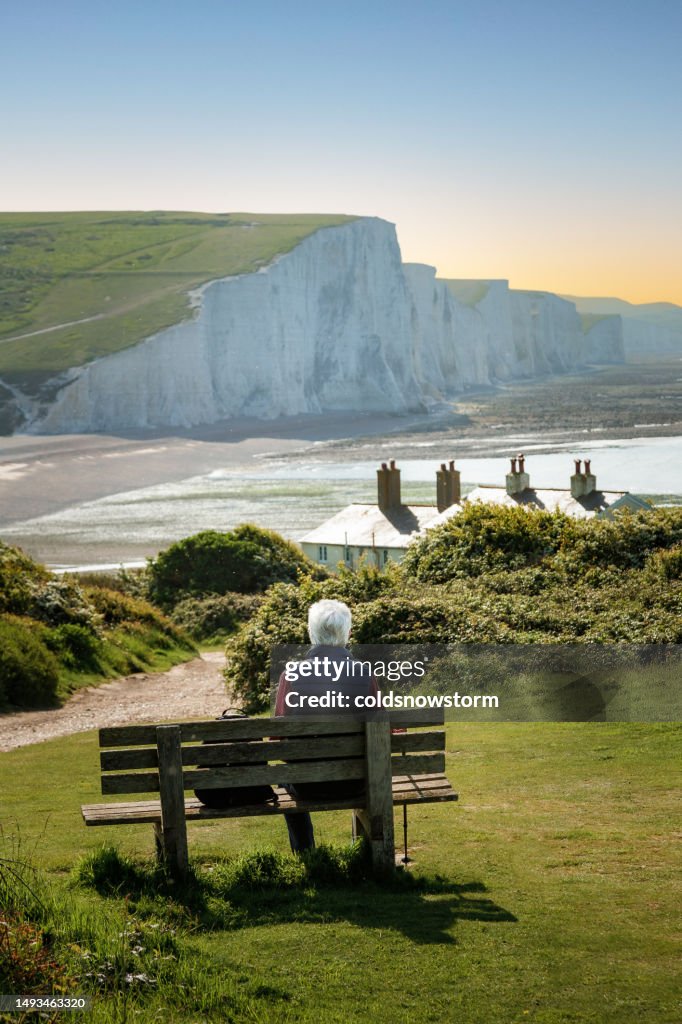 Senior man sitting on bench looking at view of Seven Sisters cliffs on south coast of England