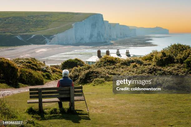 älterer mann, der auf bank sitzt und blick auf die klippen der seven sisters an der südküste englands wirft - sussex südostengland stock-fotos und bilder