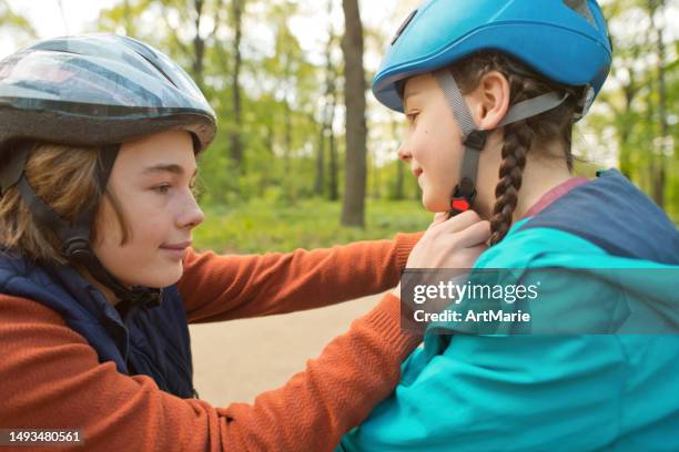 boy helps his sister to put on helmet before roller-skating and riding scooter - crash helmet stock pictures, royalty-free photos & images