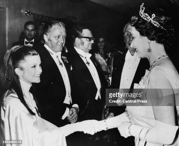 Queen Elizabeth II shakes hands with actress Genevieve Bujold, actor Richard Attenborough and comedian Harry Secombe standing beside her during the...