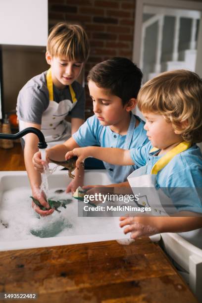 恐竜のおもちゃを洗い、台所の流しで遊ぶ子どもたち - 動物のおもちゃ ストックフォトと画像