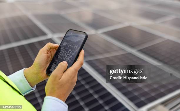 engenheiro verificando a atividade de painéis solares em um telhado usando um telefone celular - power supply - fotografias e filmes do acervo