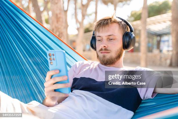 a man listening to music in a hammock on the beach - young man listening music and relaxing in hammock stock pictures, royalty-free photos & images