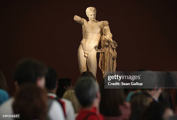 Visitors look at a statue of Hermes in the archeological museum at the site of ancient Olympia on July 26, 2012 in Olympia, Greece. The original...