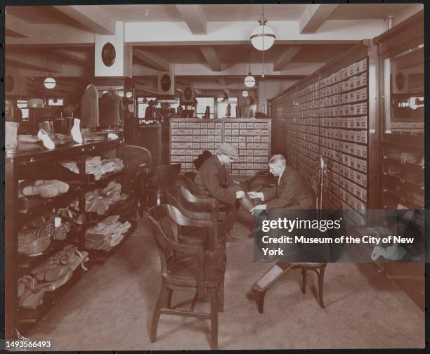 View of customer, assisted by a salesman, as he tries on socks in the Abercrombie & Fitch Co sporting goods store , New York, New York, 1913.