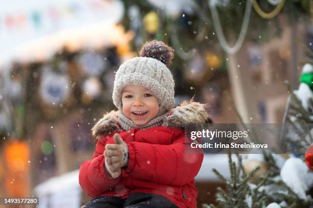 portrait of a little boy in a winter hat and jacket on the background of a christmas decoration.the kid laughs, has fun and catches snowflakes.winter fun in the christmas holidays - tumvante bildbanksfoton och bilder