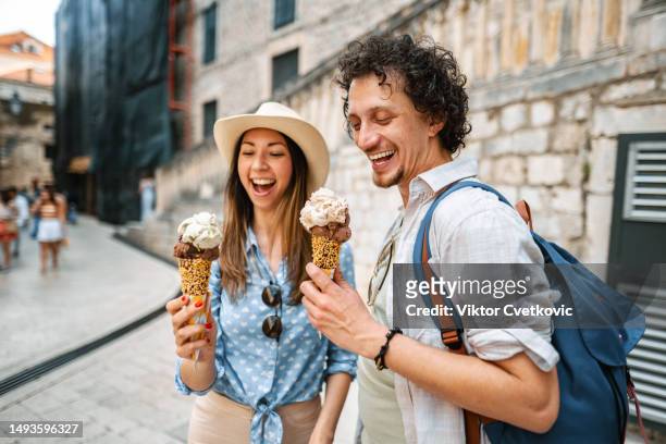 junges touristenpaar, das eis isst, während es die stadt erkundet - freundinnen urlaub sommer eis stock-fotos und bilder