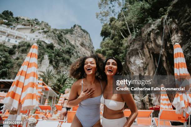 two beautiful young woman look thrilled to be standing on a sunny beach in paradise - woman towel beach stock pictures, royalty-free photos & images