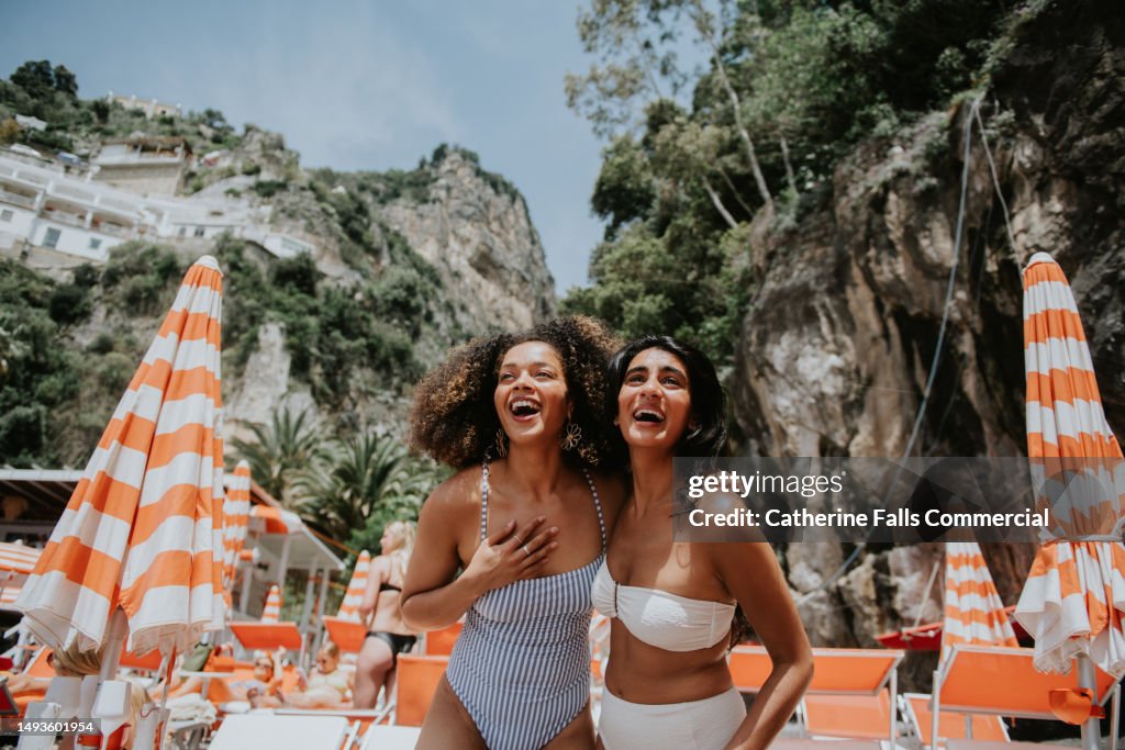 Two beautiful young woman look thrilled to be standing on a sunny beach in paradise