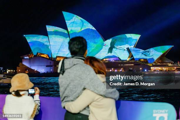 People watch the sails of the Sydney Opera House illuminated with artworks by the late Australian artist John Olsen at the start of the Vivid Sydney...