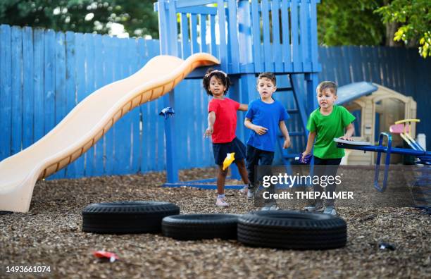 three preschool children are having fun playing a bean bag tossing game together on the playground of their daycare - playing corn hole stock pictures, royalty-free photos & images