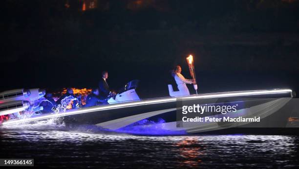 David Beckham passes under Tower Bridge driving a speedboat named 'Max Power' which carries the Olympic Torch carried by torchbearer Jade Bailey on...