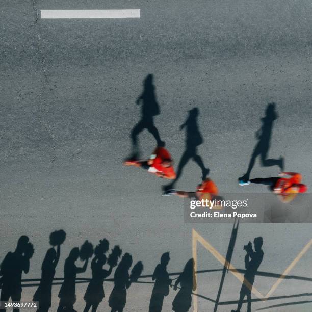 small group of triathletes running fast marathon distance and greeting fans. high angle view, square image, focused on shadow - cameraman grey background stock pictures, royalty-free photos & images