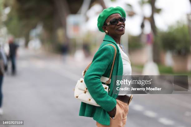 Guest seen wearing a green hat, black sunglasses, a white blouse, a green blazer, beige pants and black loafer shoes during the 76th Cannes film...