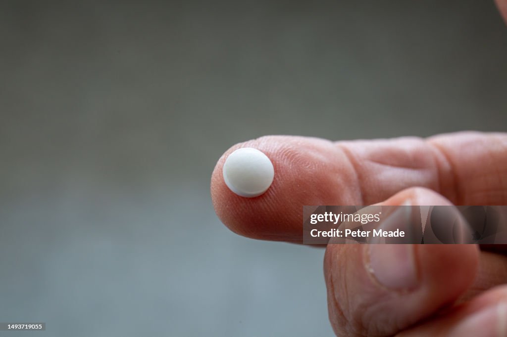 A low dose aspirin pill resting on a human finger
