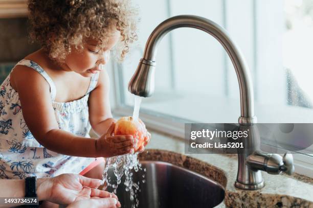 cute toddler with mom together at home washing apples in the sink, domestic life - food waste stockfoto's en -beelden