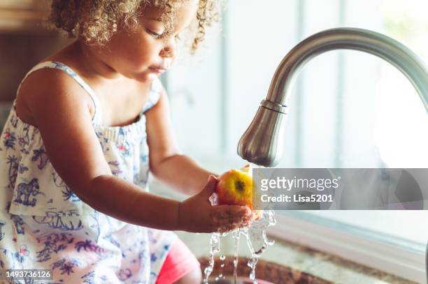 cute toddler at home washing apples in the sink, domestic life - running water faucet stock pictures, royalty-free photos & images